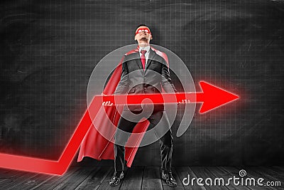 Businessman wearing red superman mask and cloak holding red diagram arrow on black background. Stock Photo