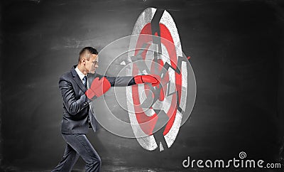 A businessman wears boxing gloves and breaks a chalk drawing of a round archery target. Stock Photo