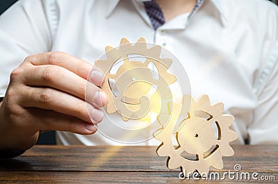 Businessman in white shirt connects two wooden gears. Symbolism of establishing business processes and communication. Increase Stock Photo