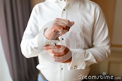 Businessman in a white shirt straightens cuffs, standing at the window in natural light. Man buttons cuff-link on French cuffs sle Stock Photo