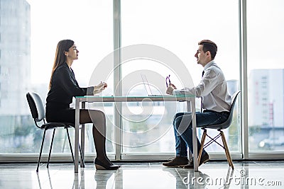 Businessman and woman having a discussion in the office face to face at table against windows Stock Photo