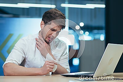 A businessman at work is sick, coughs and has a runny nose, sits at a table with a napkin and sneezes Stock Photo