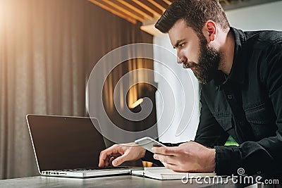 Businessman working on laptop while holding smartphone. Entrepreneur analyzes information, develops business strategy. Stock Photo