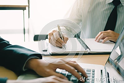 Businessman writing in notepad while his partner using laptop co Stock Photo