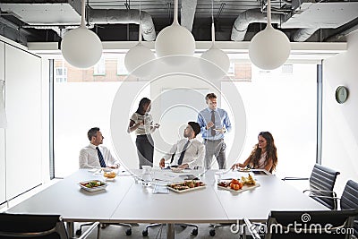 Businessmen And Businesswomen Meeting In Modern Boardroom Over Working Lunch Stock Photo