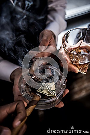 Businessmen with dollar banknote in ashtray drinking whiskey and smoking cigars Stock Photo