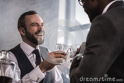 Businessmen in formal wear clinking whiskey glasses and talking Stock Photo