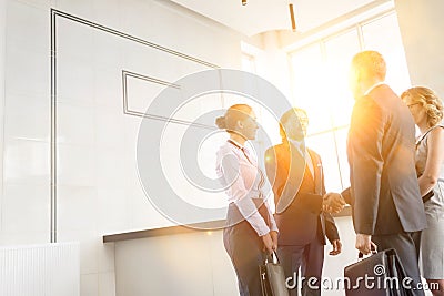 Businessmen greeting while standing with colleagues at reception lobby in office and yellow lens flare in background Stock Photo