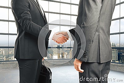 Businessmen shake hands in empty loft style room with glassy win Stock Photo