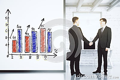 Businessmen shake hands in loft office with white wall with business graph Stock Photo