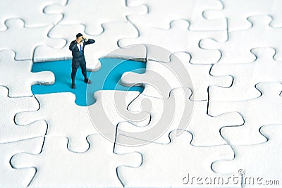 Businessmen standing above missing jigsaw puzzle using binoculars. Miniature tiny people toys photography Stock Photo