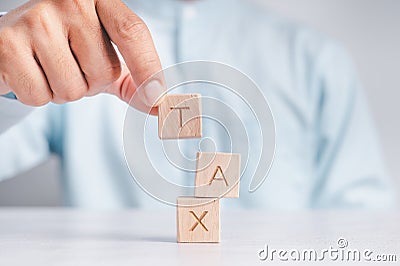 Businessmen wear a white shirt at their desks in the office. Use your hand to pick up a wooden cube inscribed with the word tax Stock Photo