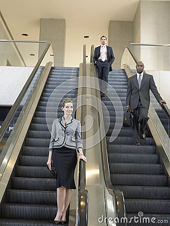 Businesspeople Moving Down On Escalator In Office Stock Photo