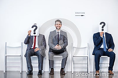 Businesspeople sitting in queue and waiting for interview, holding question marks in office Stock Photo