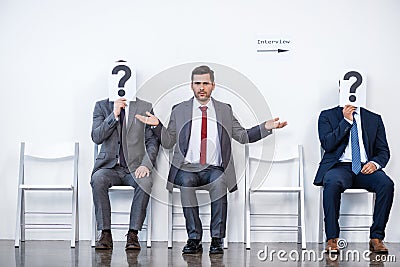 Businesspeople sitting in queue and waiting for interview, holding question marks in office Stock Photo