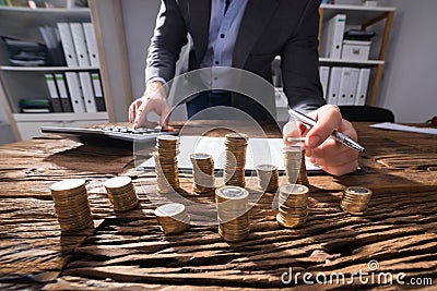 Businessperson Calculating Stacked Coins Stock Photo