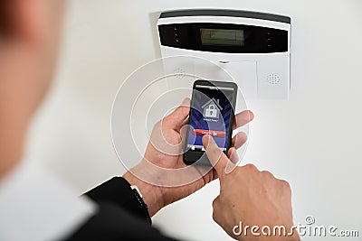 Businessperson Disarming Security System With Mobile Phone Stock Photo