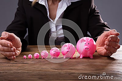 Businessperson`s Hand Protecting Piggybanks Stock Photo