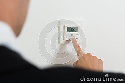 Businessperson Setting Temperature On Digital Thermostat Stock Photo