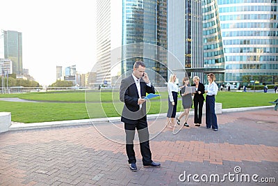 Businessperson talking by smartphone with employees in backgroun Stock Photo