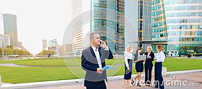 Businessperson talking by smartphone with employees in backgroun Stock Photo
