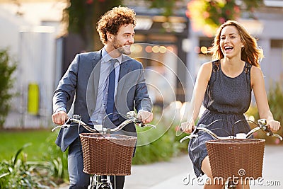 Businesswoman And Businessman Riding Bike Through City Park Stock Photo