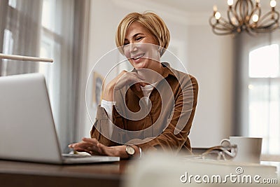 Businesswoman. Female With Laptop. Mature Blonde Woman In Brown Jacket Sits At The Desk With Computer And Cup. Stock Photo