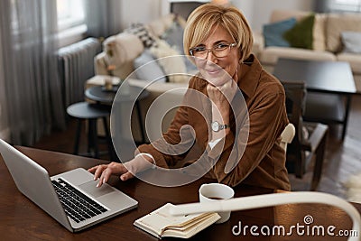 Businesswoman. Female Uses Laptop. Mature Woman Remote Homework Concept. Older Model in Brown Jacket And Eyeglasses. Stock Photo