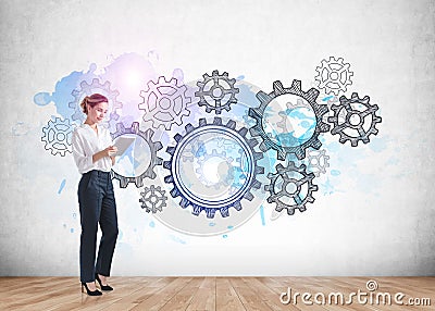 Businesswoman in formal wear holding tablet device. Parquet floor and concrete wall with colourful cogwheels and gears doodle. Stock Photo