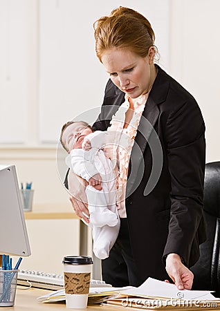 Businesswoman holding baby at desk Stock Photo