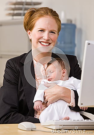 Businesswoman holding baby at desk Stock Photo