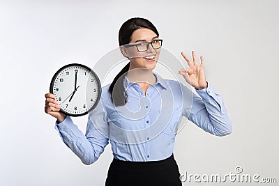 Businesswoman Holding Clock Gesturing OK On White Studio Background Stock Photo