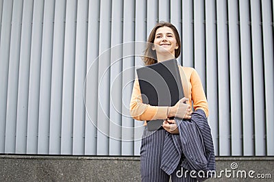 Businesswoman with laptop stay in the city against the background of the wall, a girl in a striped suit using computer outdoors Stock Photo