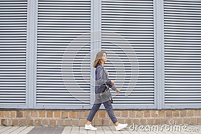 Businesswoman in the morning goes to work in the city against the background of the wall, a girl in a striped suit walks along the Stock Photo