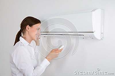 Businesswoman Operating Air Conditioner Stock Photo