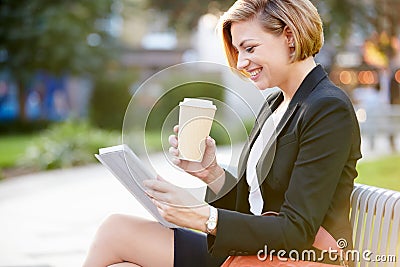 Businesswoman On Park Bench With Coffee Using Digital Tablet Stock Photo