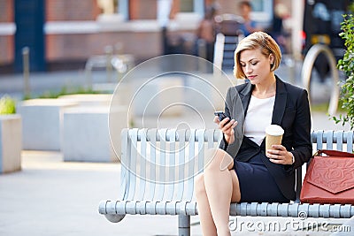 Businesswoman On Park Bench With Coffee Using Mobile Phone Stock Photo
