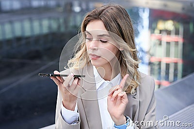 Businesswoman records voice message, dictating something on mobile phone, making a note on smartphone app Stock Photo