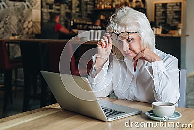 Businesswoman sits at table in front of laptop and looks closely at monitor, raising her glasses. Education for adults Stock Photo