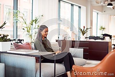 Businesswoman Sitting On Sofa Working On Laptop At Desk In Shared Workspace Office Stock Photo