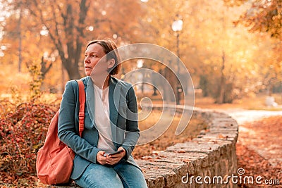 Businesswoman sitting and waiting on someone in autumn park Stock Photo