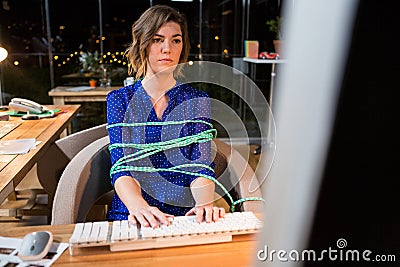 Businesswoman tied with rope while working on computer at her desk Stock Photo