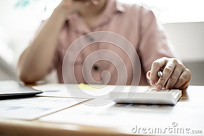 Businesswoman is using a calculator to check the numbers on a company financial document during a meeting with shareholders. Stock Photo