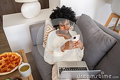 Businesswoman using phone while lying on sofa with laptop Stock Photo