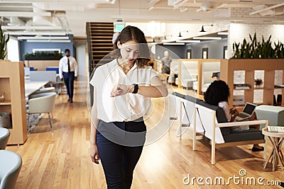 Businesswoman Walking Through Modern Office Checking Health Data On Smart Watch Stock Photo