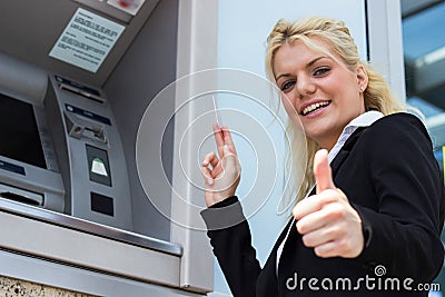 Businesswoman withdrawing money from credit card at ATM and showing okay sign Stock Photo