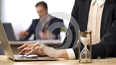 Businesswoman working on computer, hourglass trickling, outcome anticipation Stock Photo