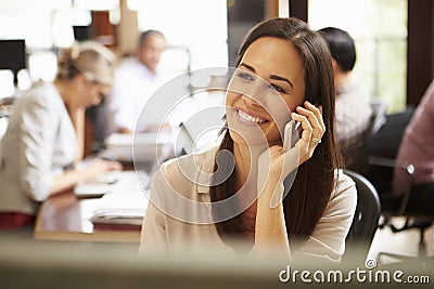 Businesswoman Working At Desk Using Mobile Phone Stock Photo