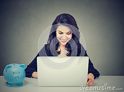 Businesswoman working with laptop computer sitting at desk with piggy bank Stock Photo