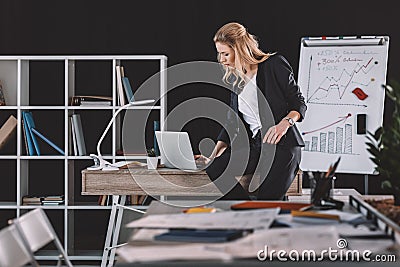 Businesswoman working in office, whiteboard with graphics and charts behind Stock Photo